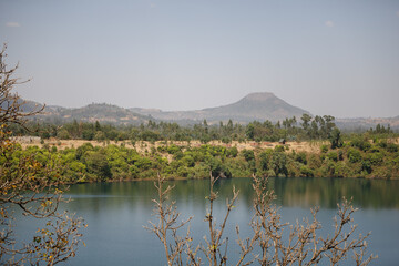 Obraz na płótnie Canvas little lake in southern ethiopia, branches are in the foreground and the other side of the lake you can see the steep shore where the trees grow