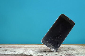 Smartphone falling and crashing on wooden surface with blue background, Accident with a smartphone