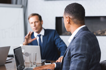 African american businessman sitting near executive gesturing at workplace during business meeting on blurred background.
