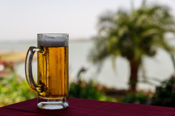 cold beer is poured into a cup that stands on the table on a very hot day and creates a refreshing feeling