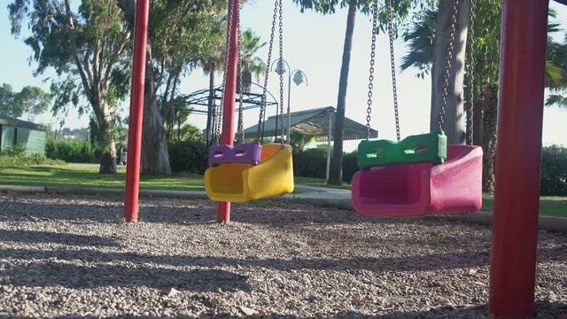 Multicolored children swing swaing by wind on empty playground in quarantine. Concept pandemic and lockdown.