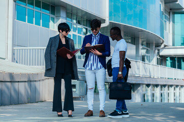 Businessman showing documents to his multi-ethnic co-workers in front of their big modern office building