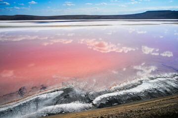 Aerial view of a pink-colored salt lake. Clouds are reflected on the pink surface of the lake.
