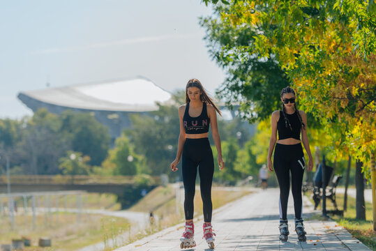Two beautiful sportswomen roller skating in the park on a sunny day