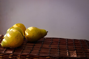 Several ripe yellow pears stand on a wicker basket illuminated by rays of the sun