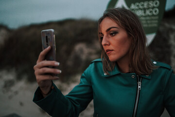  Chica rubia feliz en una playa de otoño invierno al sur de españa haciendo selfie vestida a la...