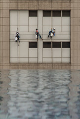 Group of workers cleaning windows service on high rise office building with reflection from swimming pool. Selective focus.
