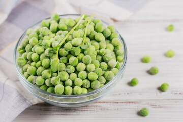 Composition with organic frozen vegetables on a white wooden background. Green peas and sprouts in a bowl.