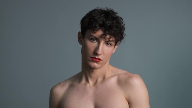 Androgyny. Transgender guy with makeup posing on grey background. Close-up. Masculine and feminine characteristics in one person. Gender identity concept 4k