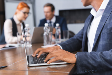 African american businessman typing on laptop at workplace with blurred colleagues on background.