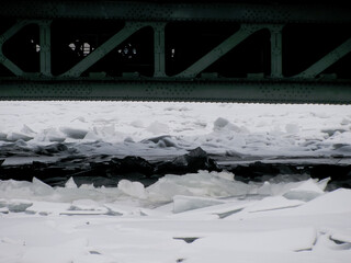 Broken ice under white snow on the river in winter under the bridge.