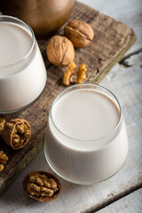 Organic walnut nuts and glass of walnut milk on wooden background.