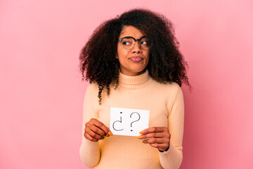 Young african american curly woman holding an interrogation on a placard confused, feels doubtful and unsure.