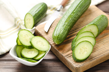 Fresh cucumbers, slices on cutting board and in bowl on brown wooden background