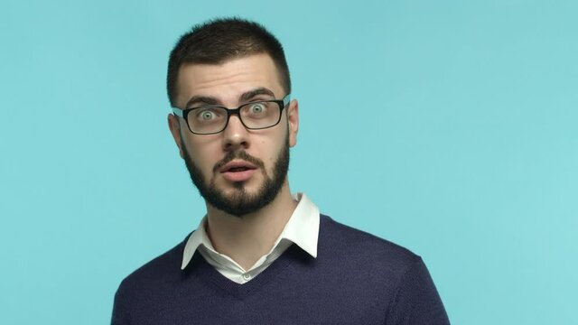 Slow motion of impressed male office worker in glasses stare at camera, raising eyebrows surprised and saying wow, looking amazed, standing over blue background