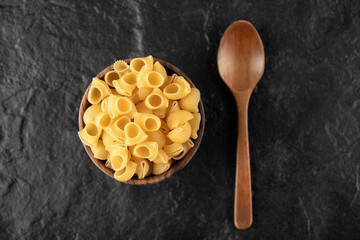 Italian uncooked pasta conchiglie in wooden bowl with a wooden spoon