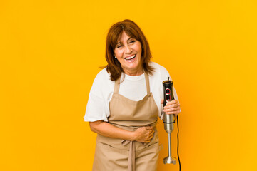 Middle age caucasian cook woman holding a mixer isolated laughing and having fun.