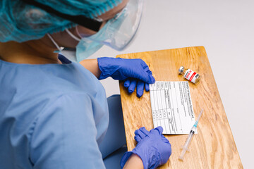 Doctor wearing PPE is held in the hands the coronavirus vaccination card. The concept of defeating...