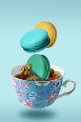 Color French macaroons falling in to the decorated blue porcelain teacup full of tea