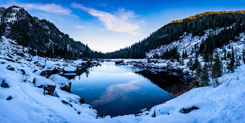 A frozen mountain lake surrounded by snow, forests and cliffs with a clear blue sky