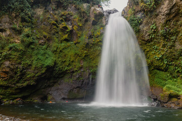 Fototapeta na wymiar A beautiful long exposure shot of a waterfall flowing through a missy rough cliff in Xico, Veracruz, Mexico