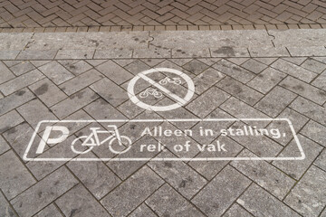 Sign of a bicycle parking on the pavement in Dutch saying "only in the marked places or racks"
