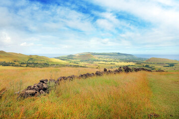 Obraz premium Panoramic view from the slopes of the Terevaka Volcano on Easter Island, showing green vegetation and the ocean against a blue sky.