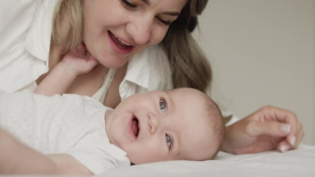 Cheerful mom kissing cute infant, admiring newborn, unconditional parental love