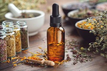 Dropper bottle of essential oil. Glass bottles of medicinal herbs. Mortar and bowls of dry herbs on...
