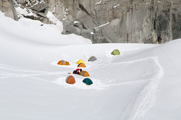 Tent base camp in the snow set in extreme high alpine environment in front of a rock face