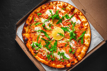 Pizza with Mozzarella cheese, salmon fish, tomato sauce, arugula, lemon. Italian pizza on Dark grey black slate background