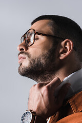 Portrait of bearded man in eyeglasses adjusting white turtleneck isolated on grey