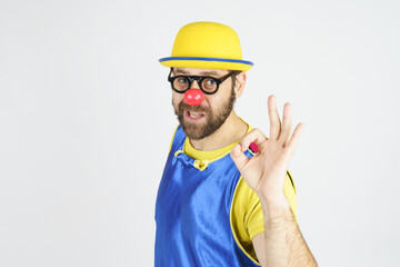 A clown in a bright blue and yellow suit, glasses and a hat shows an OK gesture