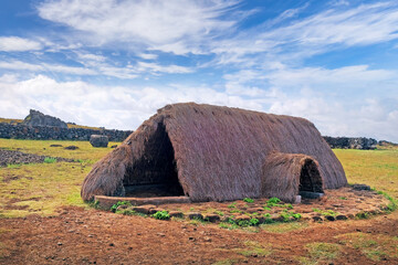Old Rapa Nui thatch-roofed house at the ceremonial center of Vaihu, on Easer Island, against a blue sky covered by white clouds.