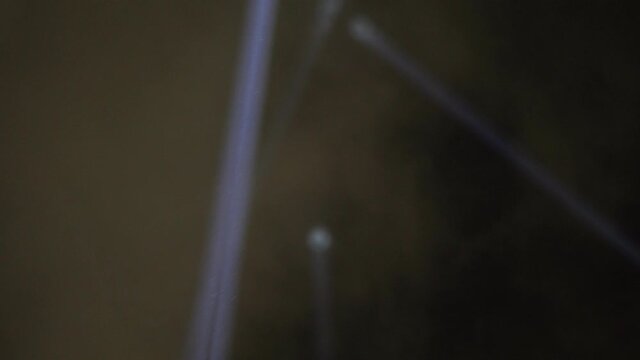 Close up on the searchlight at night. The light is very strong and illuminates the night sky.