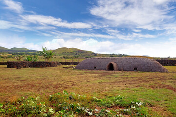 Obraz premium Old Rapa Nui thatch-roofed house at the ceremonial center of Vaihu, on Easer Island, against a blue sky covered by white clouds.