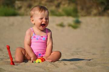 Happy baby in the sand plays. Cheerful little kid playing on the beach on a sunny day. High quality photo