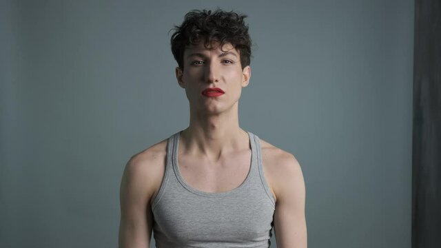 Transgender man with makeup looks at camera and wipes lipstick from his lips. Unsure feminine guy smears makeup on his face. Gender identity concept 4k