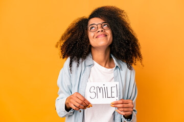 Young african american curly woman holding a smile message placard dreaming of achieving goals and...