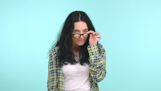 Cute young woman with long curly hair, stoop shoulders like nerd and take-off glasses, blink fast as cant see without eyewear, smiling silly, standing shy over blue background