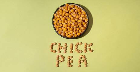 Chickpeas in small brown ceramic plate bowl isolated on a green olive background.
