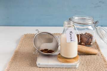 Almond milk in a bottle next to a jar and a strainer full of almonds. Horizontal view.
