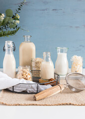 Types of alternative milks in bottles on a rustic tablecloth. Crystal jars full of seeds ,cereal and nuts are next to them. Vertical view.