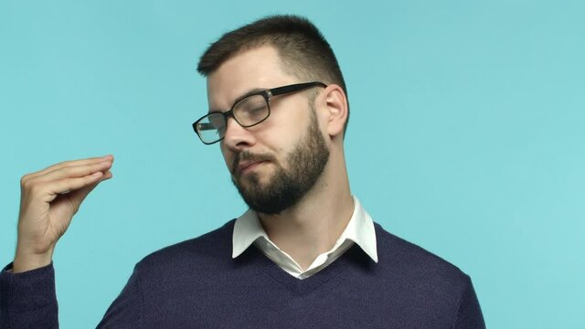 Slow motion of tired and annoyed man in glasses roll eyes, showing blah blah gesture as someone being talkative and irritating, standing over blue background