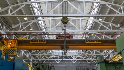 Fototapeta premium Yellow overhead crane with linear traverse and hooks in engineering plant shop. Industry concept.