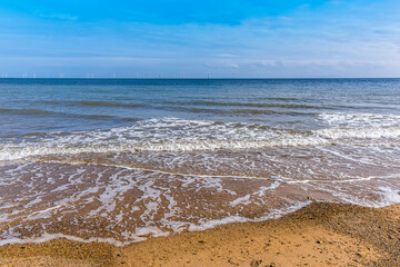 At the water's edge on Skegness beach, UK in summer with a wind farm just visible on the horizon