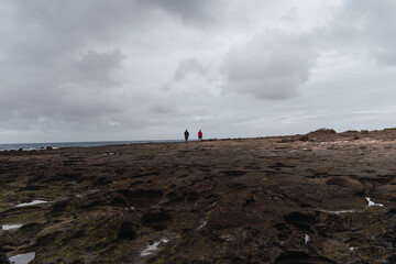 people strolling along the shore of a yellow sand beach on a cloudy day