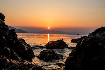 Sunrise / sunset over the sea, rocks and cliffs come out of the water with reflections of warm colors, golden hour.