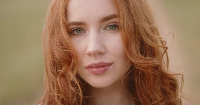 Beautiful caucasian woman with red hair and freckles is expressively looking at camera and smiling. Portrait of gorgeous woman in nature 4k footage