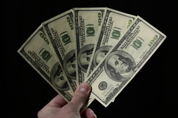 Hand holds one hundred dollar bills on black background
